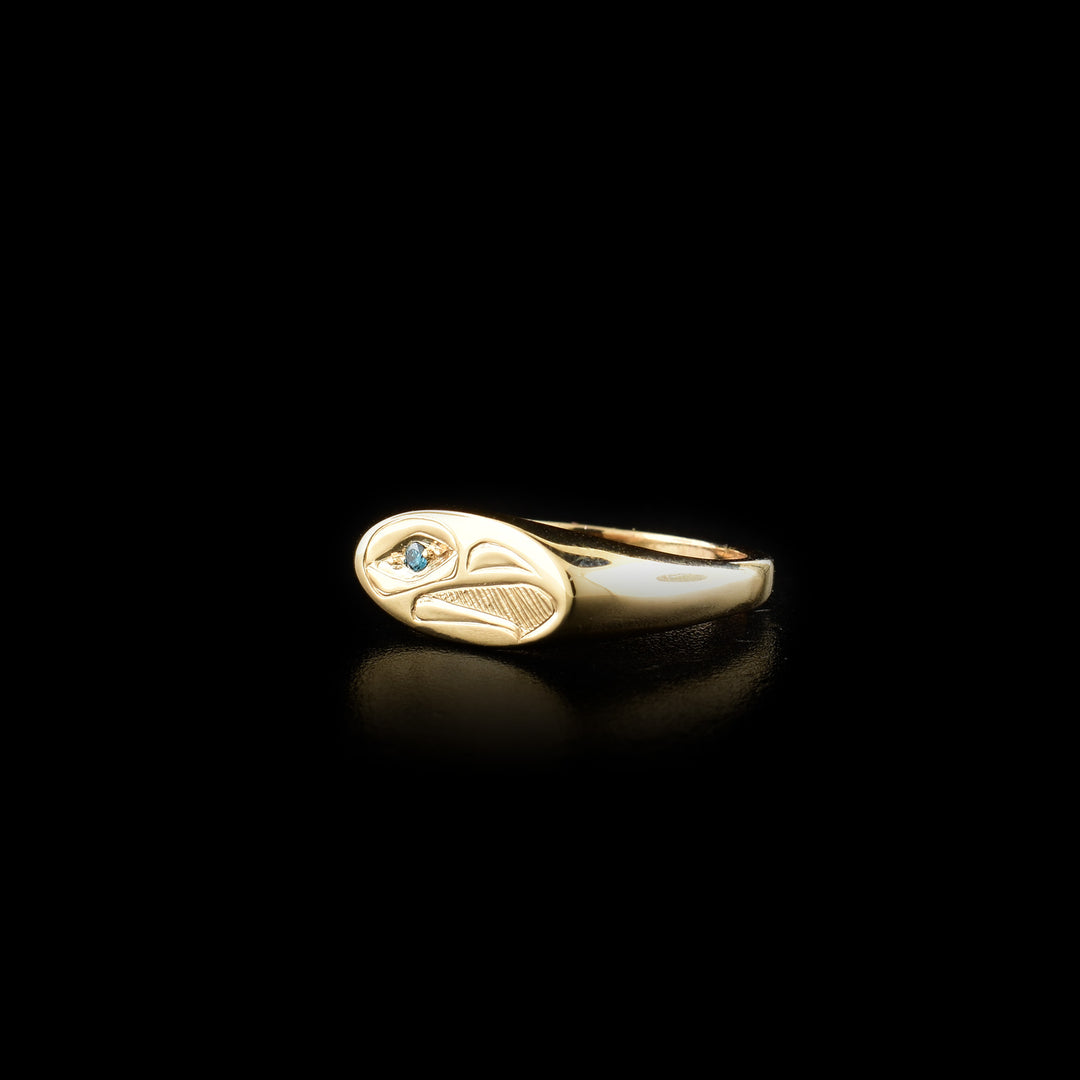 This dainty signet ring is made from 14K gold and has a thin, oval signet. The head of the Eagle is carved in a side profile into the signet. Its beak is open and there are hatching patterns made behind the head. There is a blue diamond embedded into the eye of the Eagle.