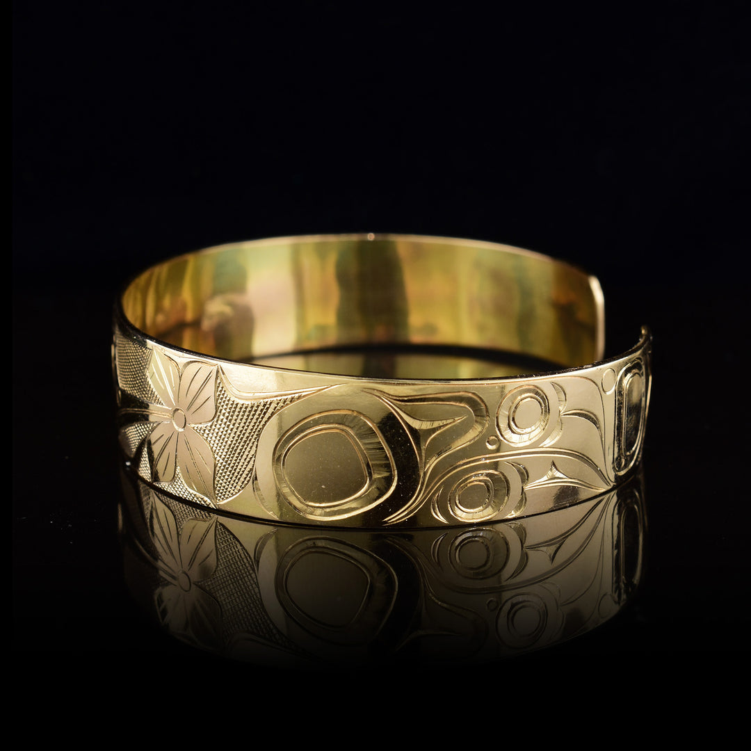 Left side of the gold cuff bracelet depicts intricate carvings representing the wings and feathers of the Hummingbird.