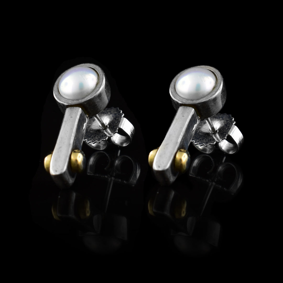 These pearl stud earrings are made from sterling silver and have a pearl held by silver with a small arm reaching down from the pearl. At the end of these arms are two 14K yellow gold beads.