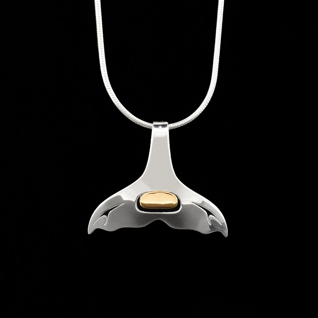 This beautiful whale tail pendant is made from sterling silver and 18K gold. The pendant is smooth and shaped like a whales tail with small cutouts at the base of the fins. There is an oval section in the middle of the tail that is made from 18K gold.