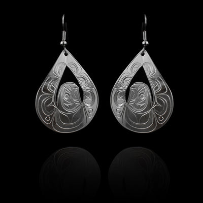 These large silver earrings have wide, teardrop shaped hangs with cutouts in the center of them. In the center of the hangs is The head of the Eagle and its wings outstretched above its head to form the teardrop shape. There are carvings on the surface of the hangs depicting the Eagle.