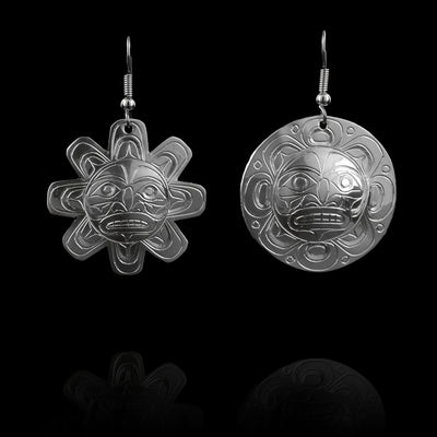 These large Sun and Moon earrings have sterling silver hangs with a round shape. One of the hangs depicts the Sun and the other, the Moon. There are carvings on both of the hangs depicting the legends and the Sun earrings it cutout in the shape of the Sun and the Moon is round.