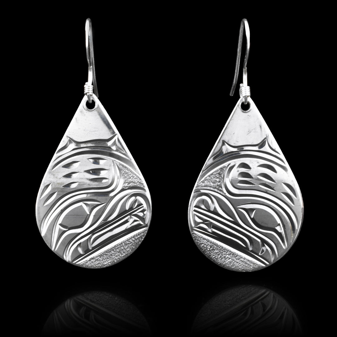 These dangling Bear earrings have teardrop shaped hangs that are made from sterling silver. There are depictions of the head of the Bear carved into the hangs. The head is done at a side profile with its nose, teeth, eye and fur details included. There are dimpled patterns in the background of the scene.