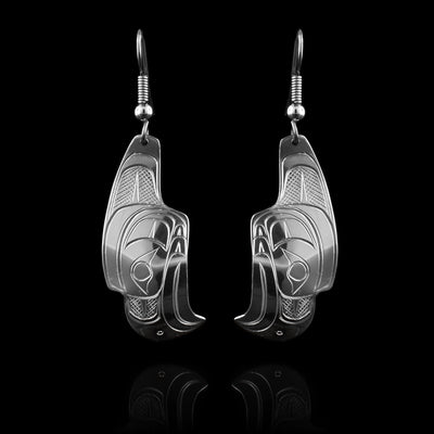 These Thunderbird earrings are made from sterling silver and have long hangs that drop down. The hangs are shaped like the side profile of the Thunderbird and have carvings on the surface of them depicting the legend. The beaks points down and there is a long, father detail at the top of the head that attached to the hooks.