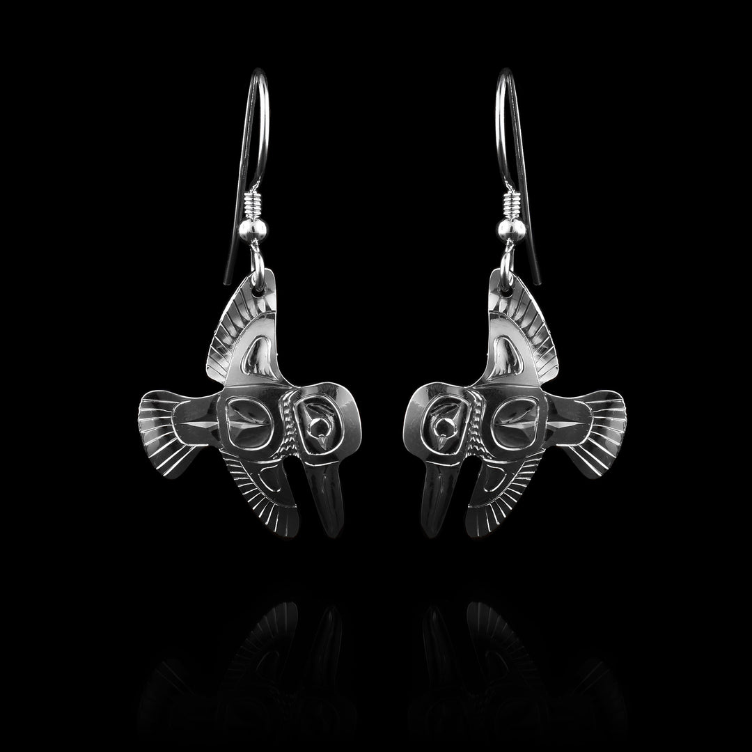 These dainty dangling Hummingbird earrings have small hangs made from sterling silver. The hangs are shaped like a hummingbird with its wings out vertically and its head is at a side profile and looking downwards. There are many feather details carved into the hangs and the eye and beak are detailed.