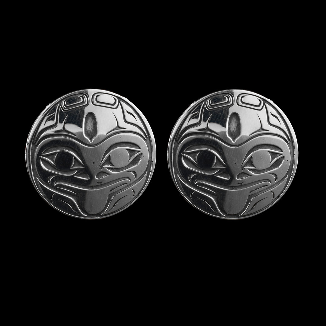 These large stud earrings are made from sterling silver and have a circle shape. The face of the frog with its tongue out is shown on the piece and there are smaller details representing its legs. The face is looking towards you and you can see both of its eyes.