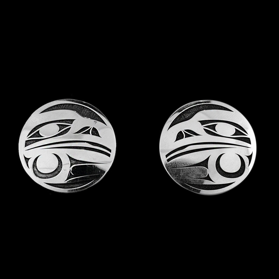 These large circle stud earrings are made from oxidized silver and sterling silver. The studs are circle shaped and there is a side profile of the of the Raven legend cast into them. The head is at the top and below the head is a feather design that represents its wing.