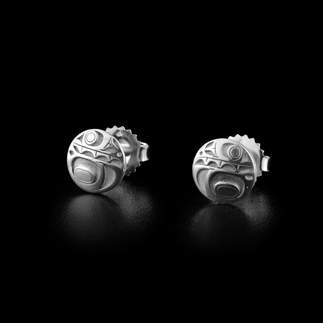 These Orca stud earrings are made from sterling silver and have a small, circle shape. The Orca legend is shown at a side profile and the carvings are deep in the surface. The head with its eye and mouth is at the top of the stud and there is a fin design below it on the bottom half.