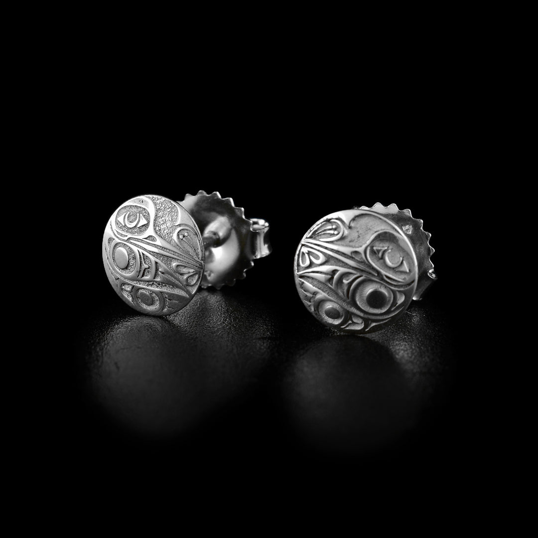 These Hummingbird stud earrings are made from sterling silver and have a small, circle shape. The Hummingbird legend is shown at a side profile and the carvings are deep in the surface. Its body is at one side of the studs with its beak extending across into the petals of a flower.