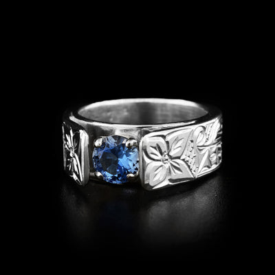This wolf ring is a classic solitaire ring with a blue stone in a silver setting in the center with two flowers carved on both sides. The band depicts the heads of two wolves on each side of the ring facing towards the stone.