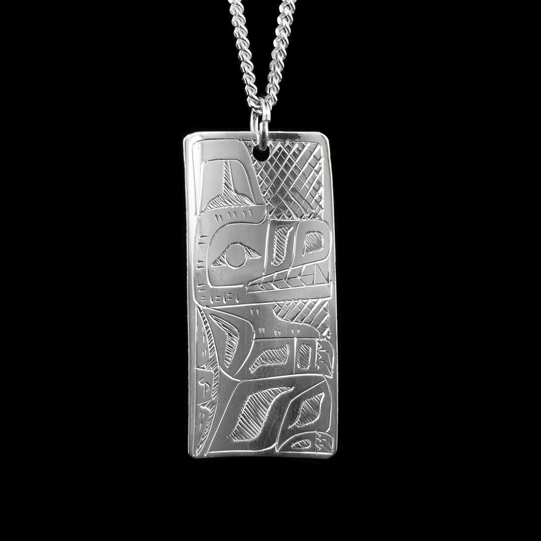 This Hummingbird and Wolf pendant is made from sterling silver and has a wide, rectangular shape to it. This piece is double sided and there is a depiction of the Wolf carved into one side and a depiction of the Hummingbird carved into the other.
