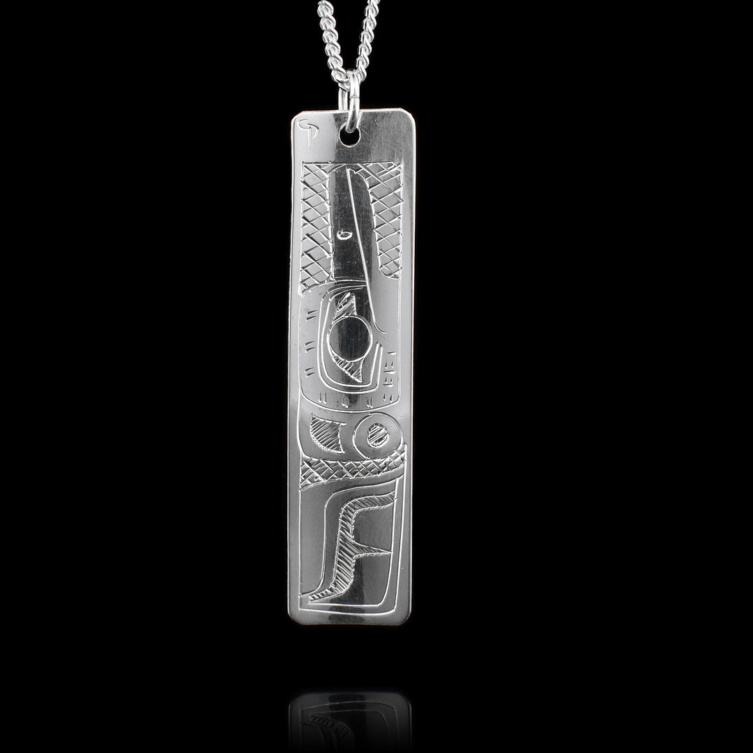 This Hummingbird and Orca pendant is made from sterling silver and has a long, thin and rectangular shape to it. There are designs on both sides of the piece, on one side there is a depiction of the Orca carved into it and on the other there is a depiction of the Hummingbird.