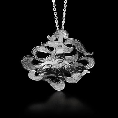 This orca pendant depicts a side-view of an orca swimming in waves. Orca is attached to waves background and its design is done in ovoids and lines. The waves twist and turn behind the orca like ribbon with a cross-hatching design.
