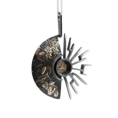 This oxidized silver necklace is circular in shape on the left side and on the right it is made up of abstract lines imitating sun rays.
