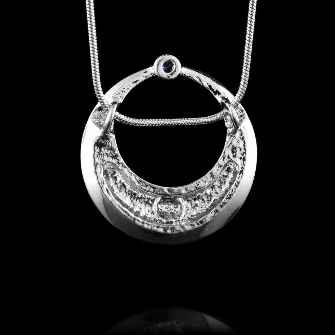 This cubic zirconia pendant necklace is made from sterling silver and has a circle shape. There is a large, circle cutout in the center with the bottom of the piece being wider than the top. There is a small, cubic zirconia gem held at the top of the piece and the bottom is slanted upwards slightly.
