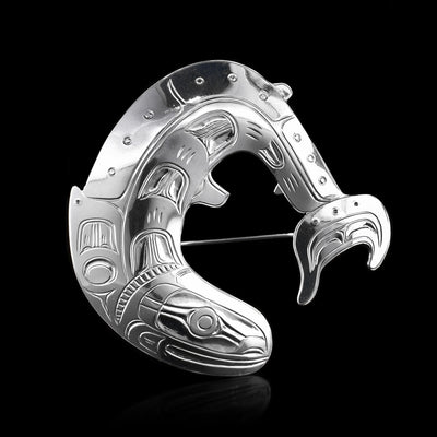 This silver brooch is shaped like a cresting salmon with intricate designs carved to represent its scales. The pin is hidden in the back.