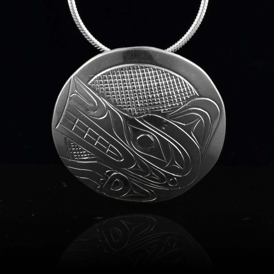 This Wolf head pendant has a small, circle shape and is made from sterling silver. The head of the Wolf is done in a side profile. The head is gazing upward and its clawed paw is below the head. There are cross hatching designs in the background of the scene.