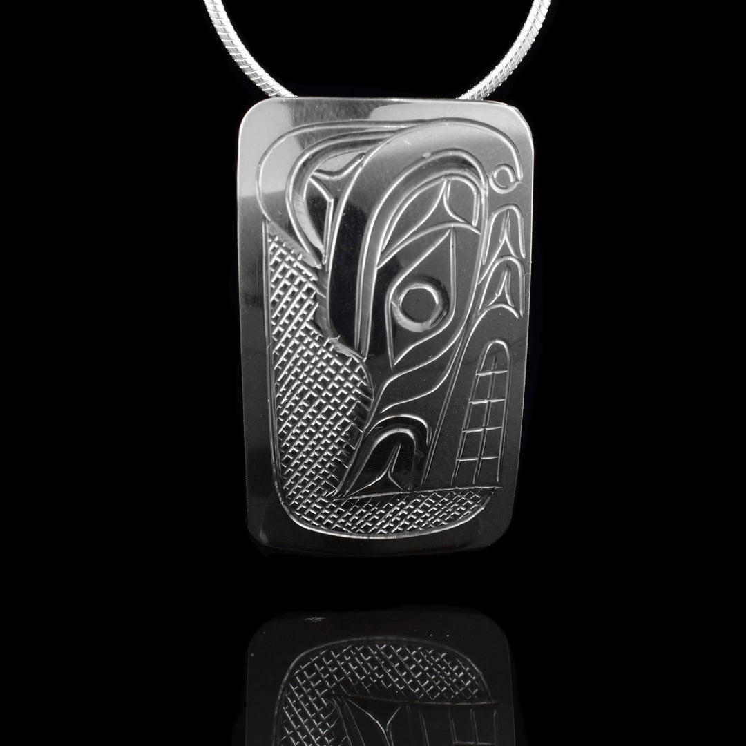 This Wolf head pendant is made from sterling silver and has a wide rectangle shape. There is a depiction of the head of the Wolf carved in a side profile on the piece. Its snout is facing down and there are cross hatching designs in the background of the scene.