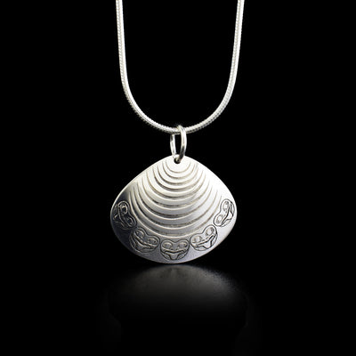 This sterling silver pendant holds the shape of a clam with faces of the Frog around the edge. 