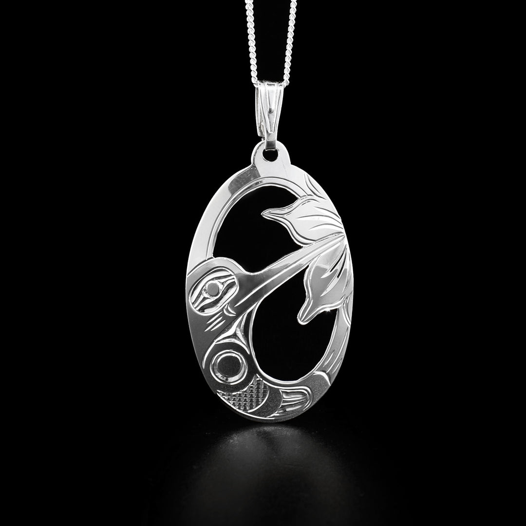 This hummingbird necklace is oval in shape and depicts the head of a hummingbird facing the left when worn drinking from a flower with its wing underneath. The background has been cut out for depth.