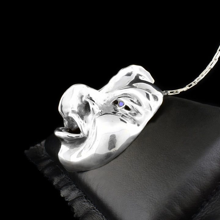 This sterling silver pendant is shaped like a face with detailed eyes, cheeks, lips, eyebrows, and nose. The are abalone gemstones set into they eyes of the mask.