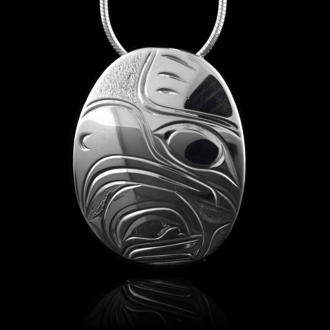 This Moon and Eagle pendant has a wide, oval shape and is made from sterling silver. There is a depiction of the head of the Eagle done at a side profile that is looking sideways and takes up most of the piece. The moon legend is depicted under the large, curved beak of the Eagle.