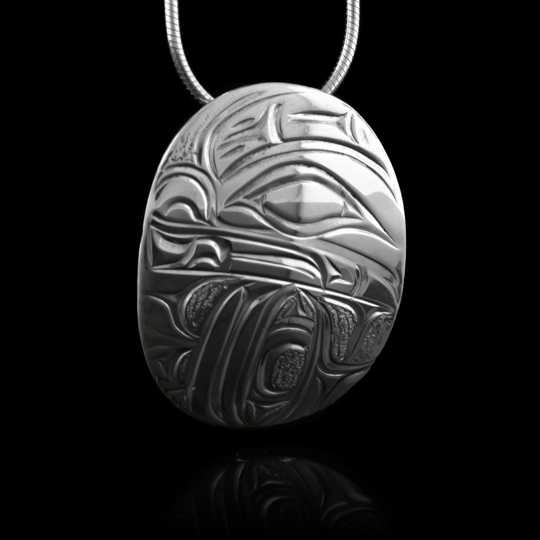 This Otter necklace pendant has a wide, oval shape and is made from sterling silver. There is a side profile depiction of the head of the Otter carved into the piece and it takes up most of the pendant. There is a sea urchin under the head of the legend.