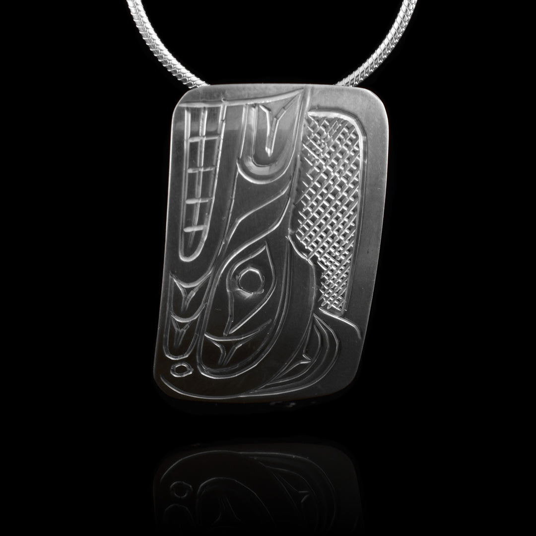 This Wolf head pendant is made from sterling silver and has a wide rectangle shape. There is a depiction of the head of the Wolf carved in a side profile on the piece. Its snout is facing up and there are cross hatching designs in the background of the scene.
