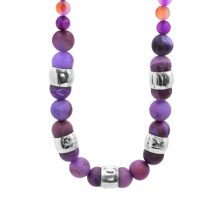 This chunky purple agate necklace has sphere shaped gemstone beads that are larger at the bottom portion of the piece and smaller at the tops of it. There are five sterling silver spirit beads that are ditributef through the large beads. The spirit beads have depictions of  the Eagle, the Moon, the Raven, the Sun and the Wolf carved into the surface of them.