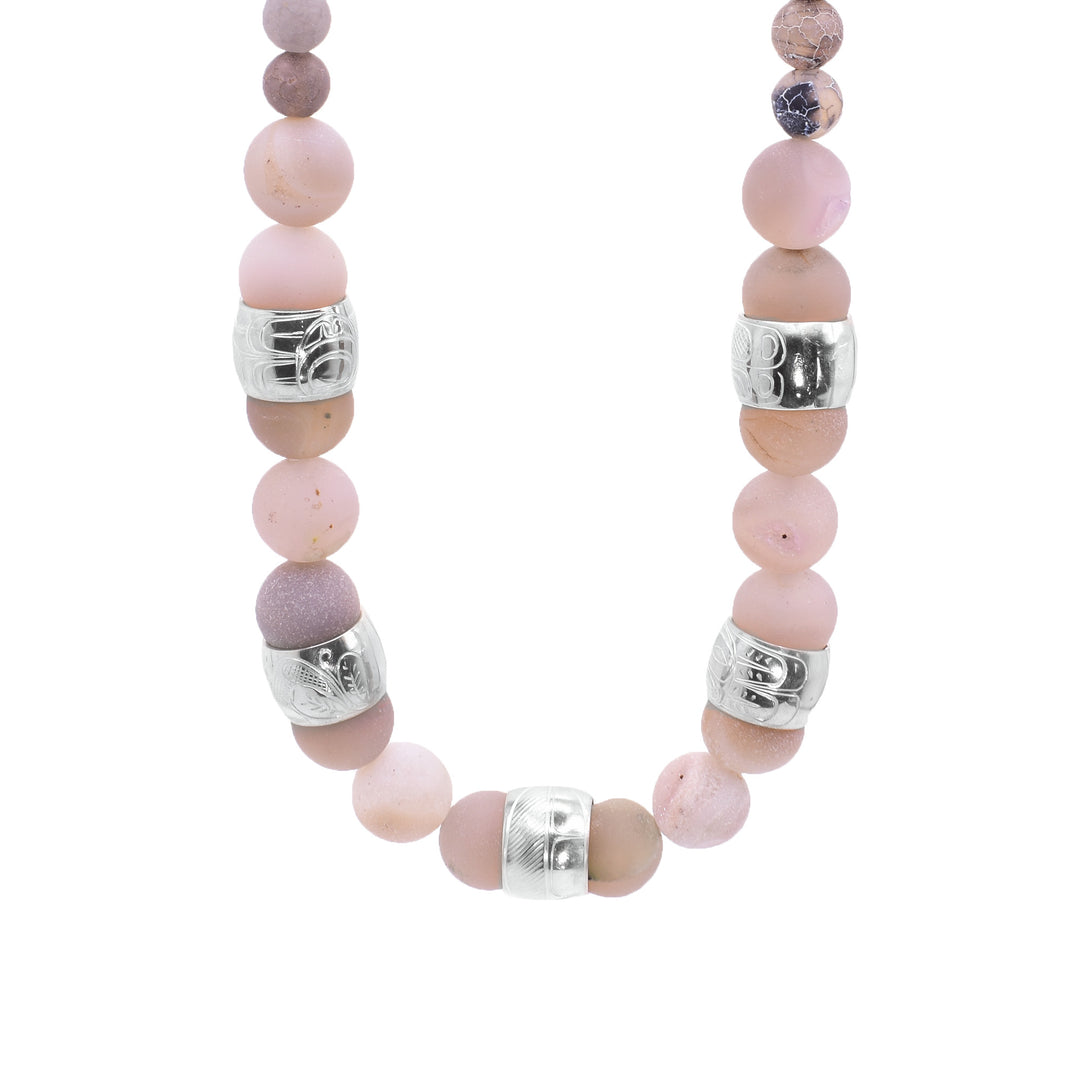 This chunky pink agate necklace has sphere shaped gemstone beads that are larger at the bottom portion of the piece and smaller at the tops of it. There are five sterling silver spirit beads that are ditributef through the large beads. The spirit beads have depictions of the Hummingbird, the Sun, the Swan, a dragonfly and a feather carved into the surface of them.