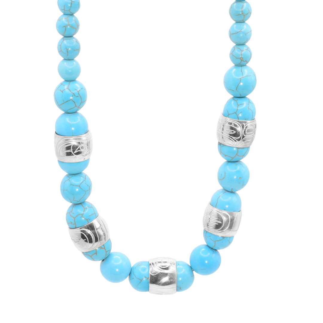This chunky turquoise necklace has sphere shaped gemstone beads that are larger at the bottom portion of the piece and smaller at the tops of it. There are five sterling silver spirit beads that are distributed through the large beads. The spirit beads have depictions of the Bear, the Orca, the Eagle, the Beaver and the Heron carved into the surface of them.