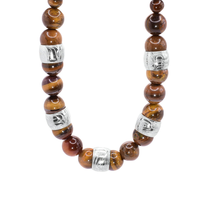 This chunky tiger's eye necklace has sphere shaped gestone beads that are larger at the bottom portion of the piece and smaller at the tops of it. There are five sterling silver spirit beads that are ditributef through the large beads. The spirit beads have depictions of the Bear, the Orca, the Eagle, the Beaver and the Heron carved into the surface of them.