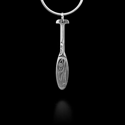 This drop pendant necklace is made from sterling silver and is shaped like a canoe paddle. The head of the Raven is depicted in a side profile on the wide portion of the paddle. The rest of the pendant is long and thin like the handle of a paddle.