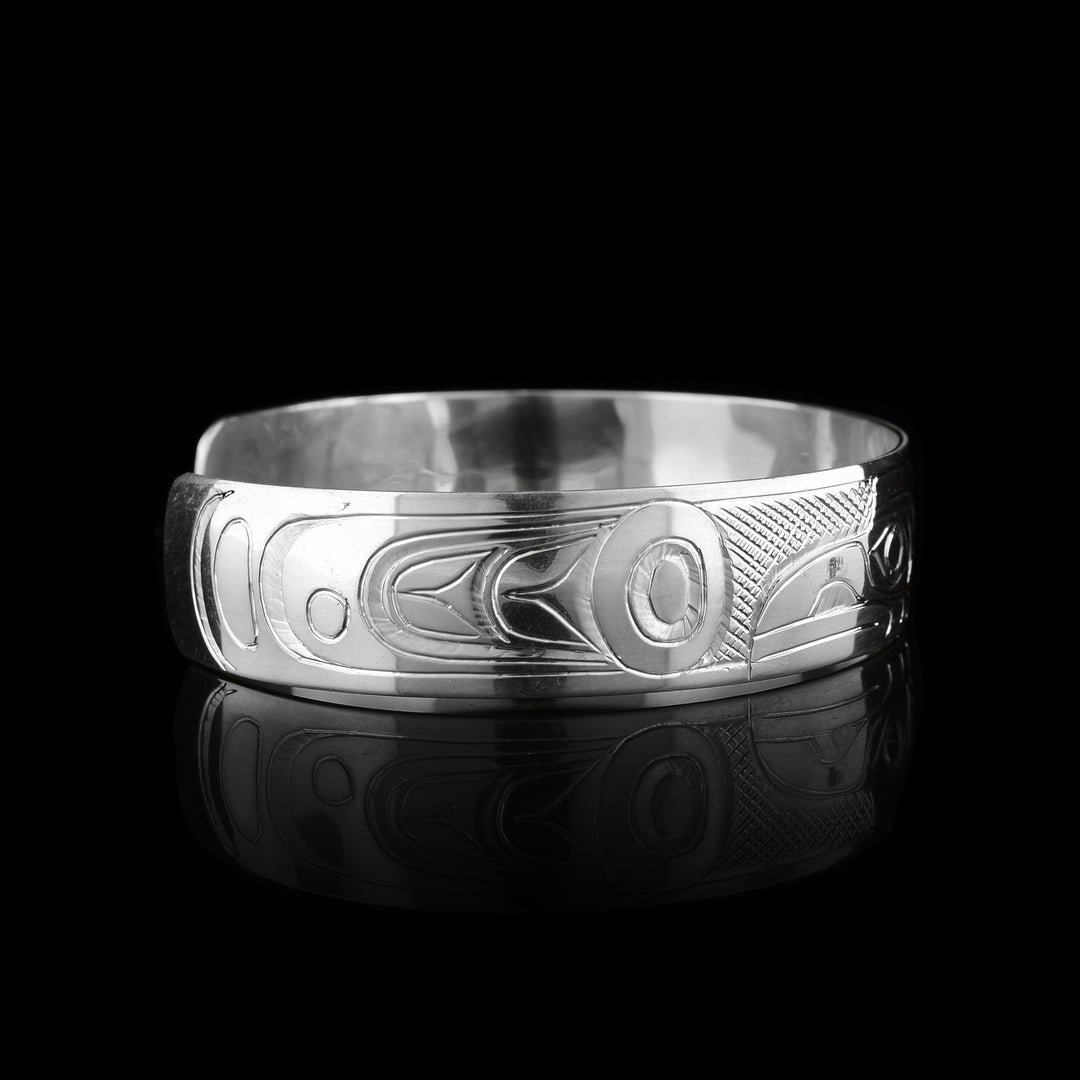 This sterling silver cuff bracelet has a single band with a gap in the back. The heads of the Raven and Eagle legend are carved into the center of the piece and are facing away from eachother. The heads take up the width of the band with the Raven on the left and the Eagle on the Right. There are circular and triangular designs depicting their wings on both the ends of the piece.