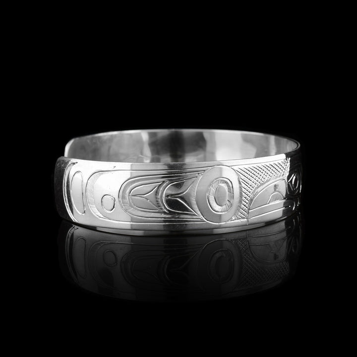 This sterling silver cuff bracelet has a single band with a gap in the back. The heads of the Raven and Eagle legend are carved into the center of the piece and are facing away from eachother. The heads take up the width of the band with the Raven on the left and the Eagle on the Right. There are circular and triangular designs depicting their wings on both the ends of the piece.