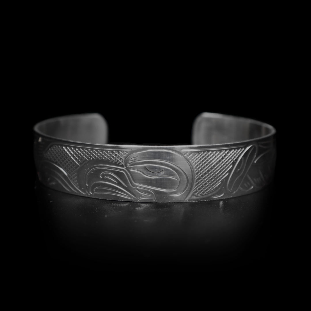 This Eagle cuff bracelet is made form sterling silver and has a depiction of the Eagle carved into the band. The head of the legend is featured in the center of the piece and its wings are outstretched across it. There are cross hatching patterns made in the negative space of the piece.