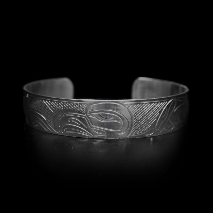 This Eagle cuff bracelet is made form sterling silver and has a depiction of the Eagle carved into the band. The head of the legend is featured in the center of the piece and its wings are outstretched across it. There are cross hatching patterns made in the negative space of the piece.