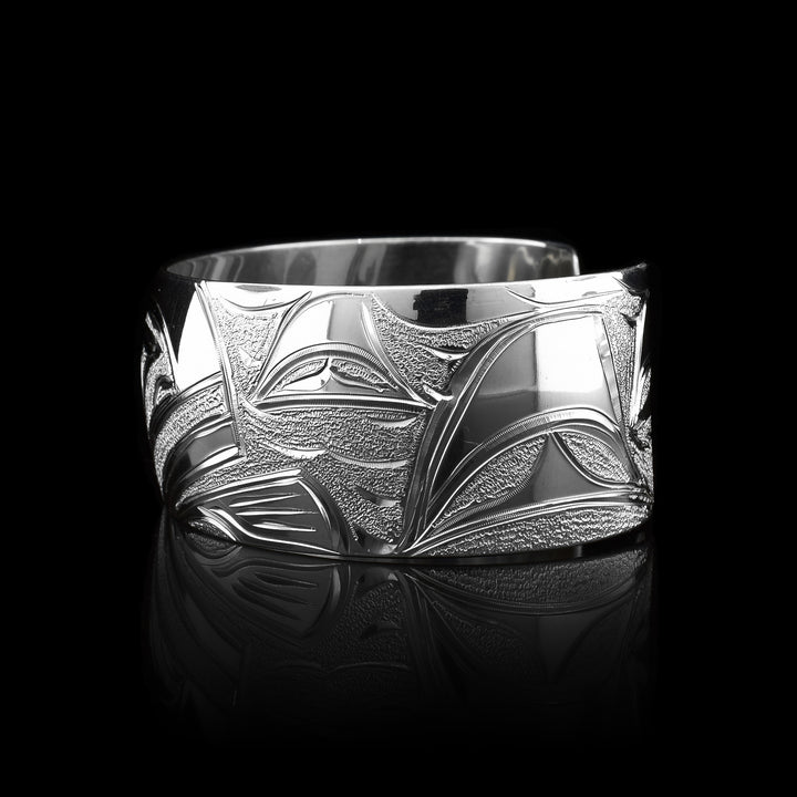 This Orca bracelet cuff has been made using sterling silver and has a single, wide band with a gap in the back. There is a gorgeous depiction of the face of the Orca and it fin carved into the center of the band. There are dorsal fins in the sea depicted on the one side of the band.
