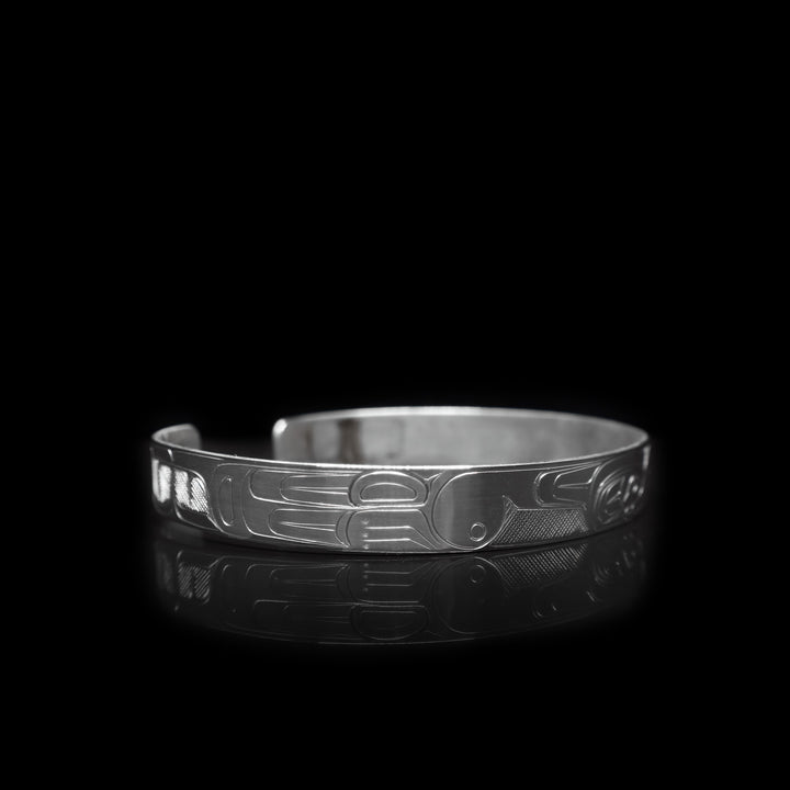 This sterling silver cuff bracelet a thin band with depictions of the Thunderbird and the Orca carved into the surface of it.