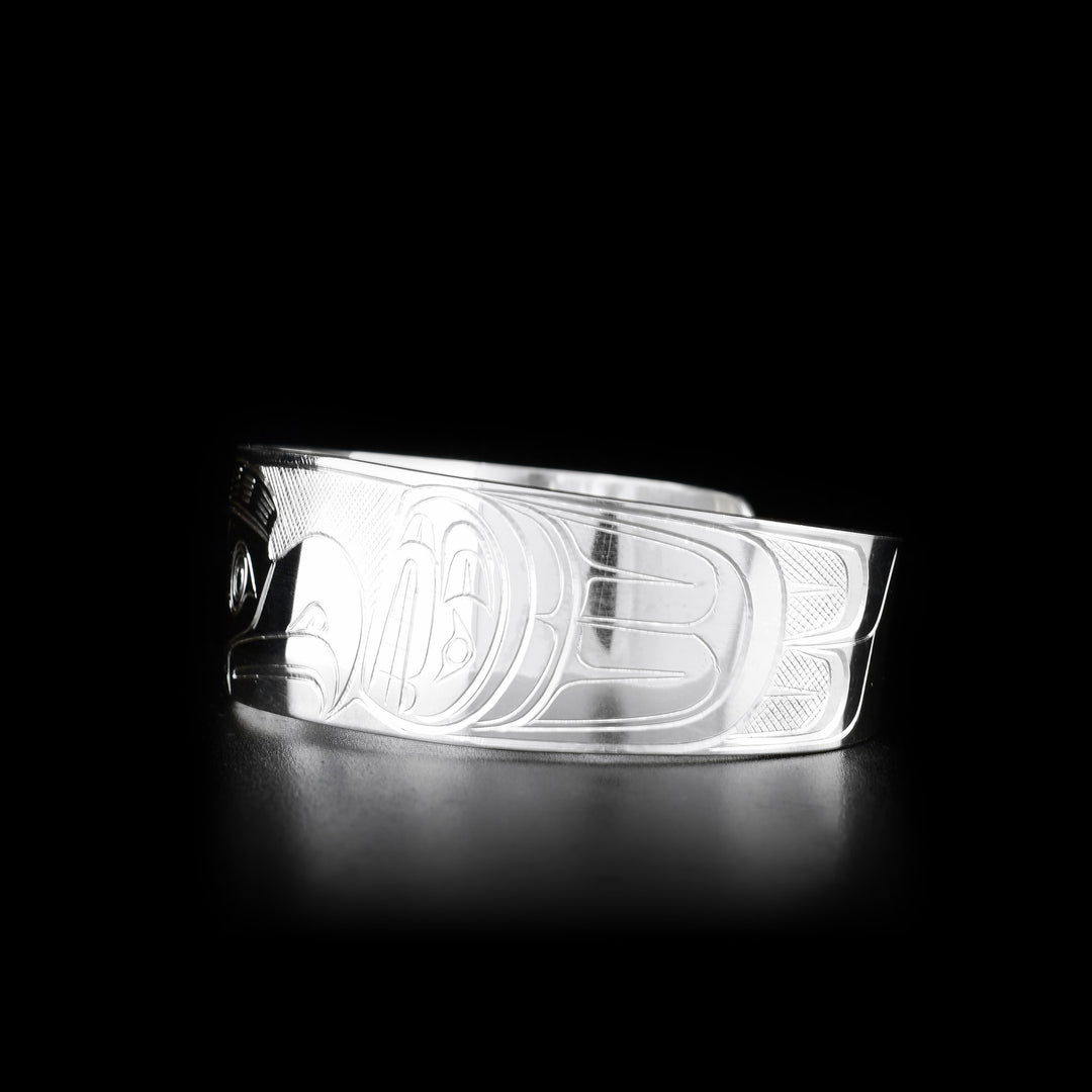 This Orca and Thunderbird bracelet cuff is made from sterling silver and has a wide band with a gap in the back. There are depictions of the Orca and the Thunderbird carved into the surface of the band.