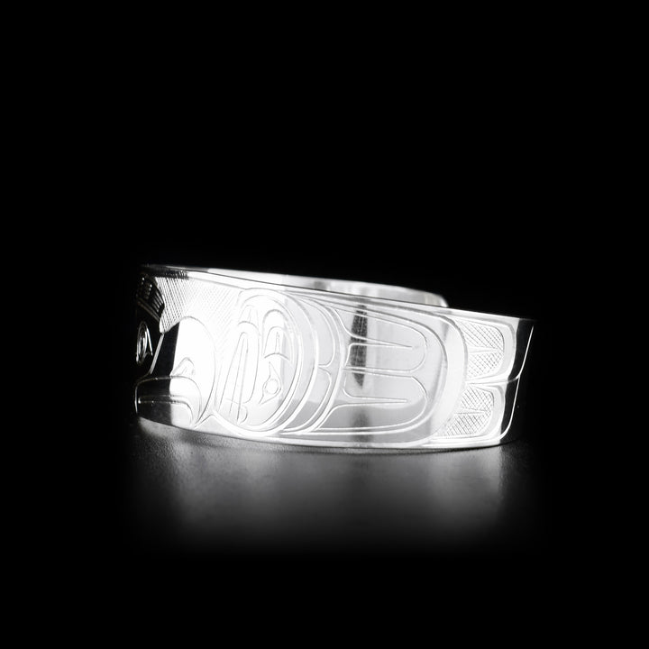 This Orca and Thunderbird bracelet cuff is made from sterling silver and has a wide band with a gap in the back. There are depictions of the Orca and the Thunderbird carved into the surface of the band.