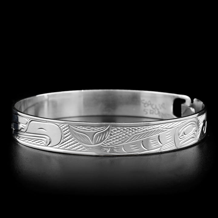 Right photo of the bracelet depicts a full-bodied salmon. In front of it are wave-like carvings.