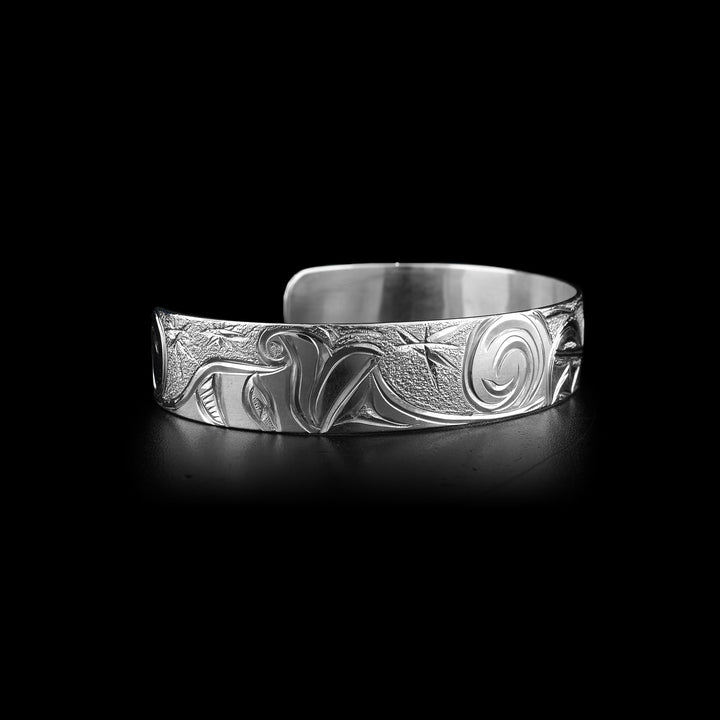 This Wolf cuff bracelet has a single band made from sterling silver with a gap in the back. The head of the Wolf is show on one half of the piece at a side profile. On the other side are swirling designs representing the night sky with stars.