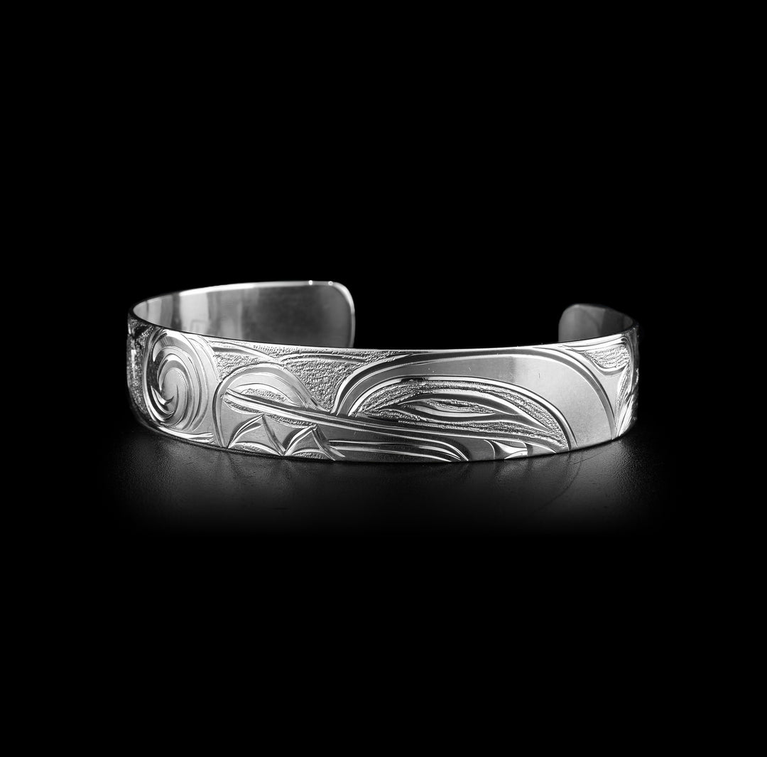 This Wolf cuff bracelet has a single band made from sterling silver with a gap in the back. The head of the Wolf is show on one half of the piece at a side profile. On the other side are swirling designs representing the night sky with stars.