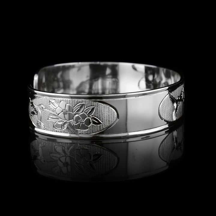 This Hummingbird with flower bracelet has a thin, sterling silver band with a gap in the back. There is a depiction of a hummingbird flying in front of rose flowers.