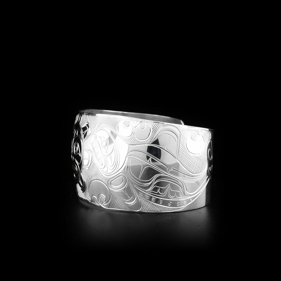This unique Orca, Sun, and Eagle bracelet is made from sterling silver and has a wide band. There is a depiction of the Sun carved into the center of the band and there are depictions of the Eagle and the Orca carved to either side of the Sun.