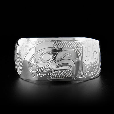 This silver cuff bracelet depicts the head of a thunderbird in the center of the bracelet facing an orca to its right. The background is cross-hatched.