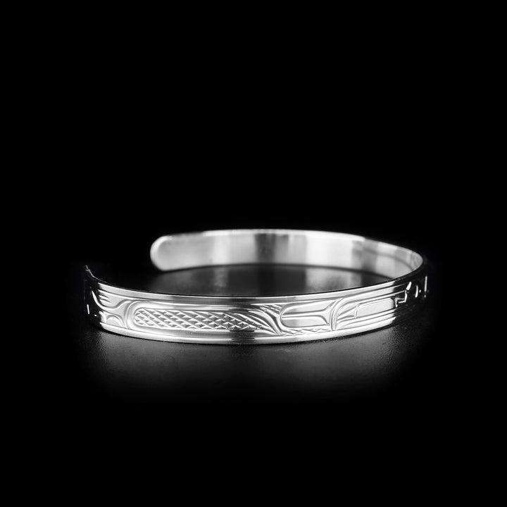 This sterling silver cuff bracelet has a thin band and is a cuff bracelet. There are depictions of the Raven and the Thunderbird carved into the surface of the band.