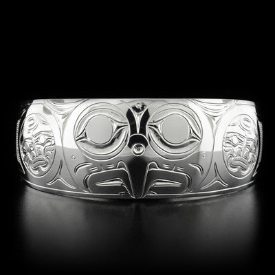 This silver bracelet has the head of an owl facing forward with a pointy beak and two large eyes in the center. On both sides are two small moons both facing forward.