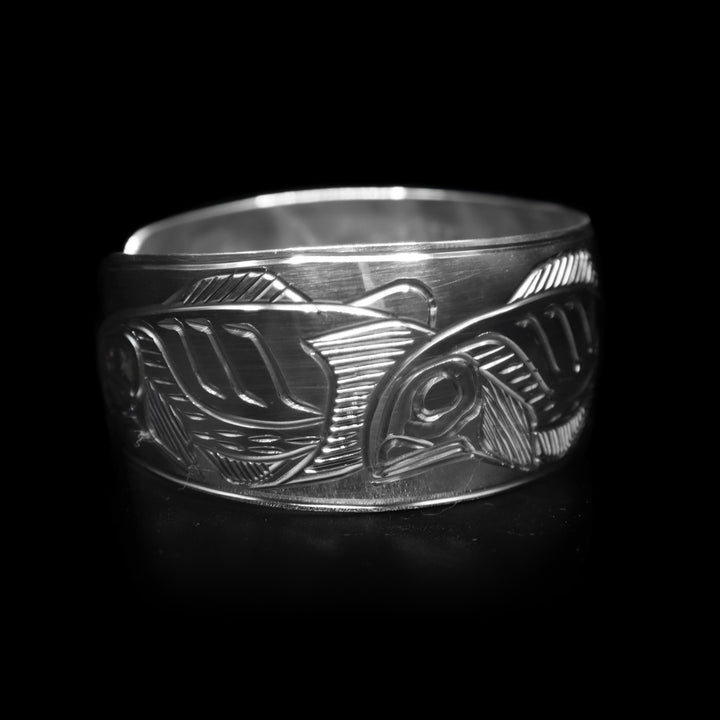 This sterling silver cuff bracelet has a wide band with a gap in the back. There are depictions of multiple indigenous legends carved into the surface of the band.
